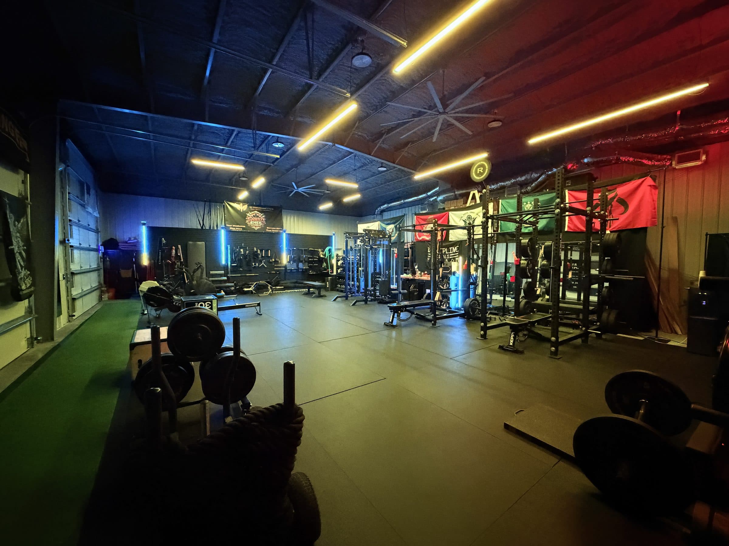 The Shred Shed training floor: racks, rig, turf lane, and free weights under the studio lights